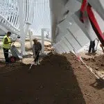 Muncitori aranjează pământul sub o structură albă modernă