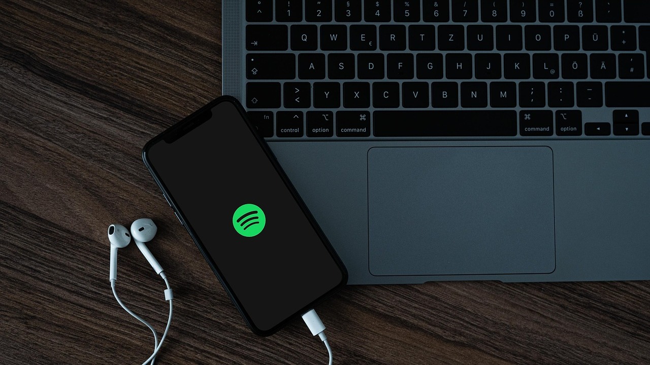 Telefon conectat la Spotify, lângă laptop și căști