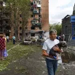 Bărbat cu câine observă clădiri distruse după bombardament