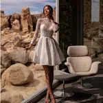 Femeie în rochie albă elegantă, stând lângă fereastră