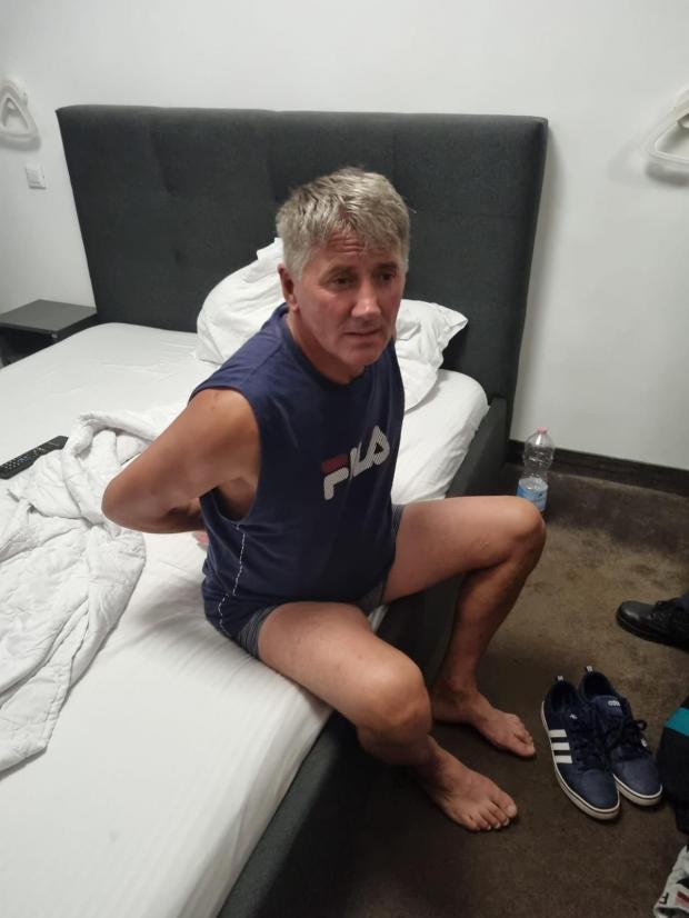Bărbat pe pat în cameră simplă, purtând tricou Fila