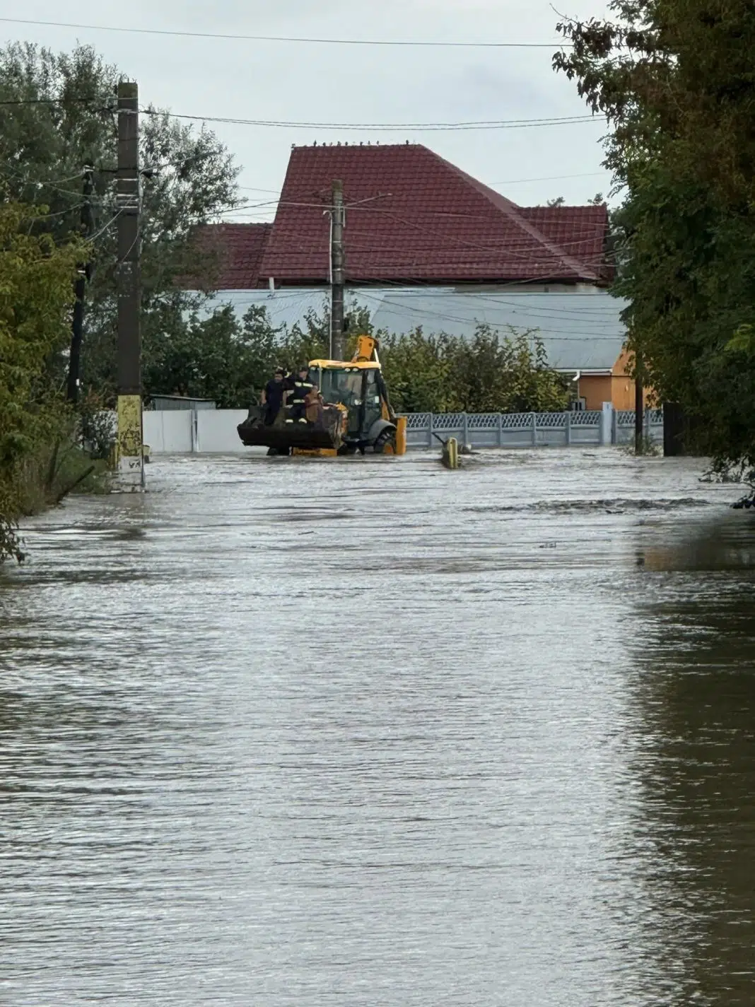 Stradă inundată cu excavator și oameni la lucru